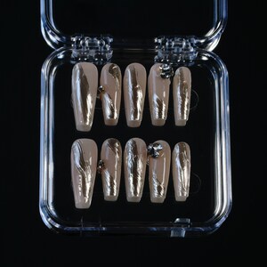 May include: A set of ten false nails in a clear plastic case. The nails are long and almond shaped with a nude base and silver foil accents. Each nail has a small clear rhinestone.