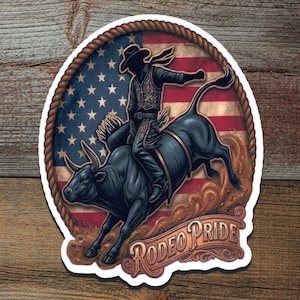 May include: A sticker featuring a rodeo scene. A cowboy rides a bucking bull against a backdrop of the American flag. The words "Rodeo Pride" are displayed in a decorative font, surrounded by a rope border.