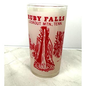 May include: A clear glass with a frosted finish, featuring red graphics and text. The text reads "RUBY FALLS LOOKOUT MTN., TENN." with illustrations of the falls. A vintage souvenir glass.