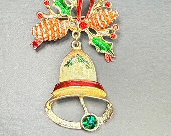 May include: A gold-toned Christmas bell brooch with red, green, and orange enamel accents. The brooch features a bell shape with a green gem, a holly and pinecone design, and a red ribbon.