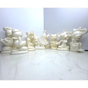 Könnte beinhalten: Eine Sammlung cremefarbener Figuren mit beliebten Zeichentrickfiguren, darunter Donald Duck, Mickey Mouse und Winnie Puuh. Die Figuren sind auf einer weißen Oberfläche angeordnet und zeigen ihre detaillierten Designs und ikonischen Posen. Die Figuren sind etwa 15 cm hoch.