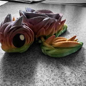 May include: A 3D printed turtle figurine with a rainbow colour scheme. The turtle's shell is made of overlapping, rose-like shapes. The turtle's head and limbs are detailed with textured scales.