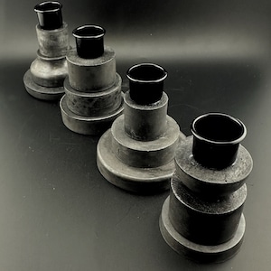 May include: Four black concrete candle holders with black metal candle cups. Each holder is a different size and has a stacked design.