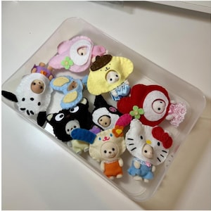 Puede incluir: Un recipiente de plástico transparente lleno de varias figuras de personajes de fieltro. Las figuras incluyen una oveja blanca, un oso negro y varios otros personajes de dibujos animados en colores brillantes. Las figuras son pequeñas y parecen hechas a mano.
