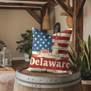 May include: A red, white, and blue pillow with a distressed American flag design. The pillow features a lighthouse and the word "Delaware" in red text.