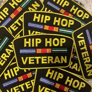 May include: Multiple black and yellow embroidered patches with the text "Hip Hop Veteran" and a colorful ribbon design.
