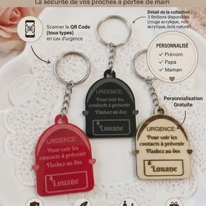 Peut inclure: Trois porte-clés d'urgence en acrylique rouge, acrylique noir et bois naturel, chacun avec un anneau métallique, un pendentif en forme de sac à dos, le texte URGENCE et le prénom personnalisé Louane, avec un QR code pour les contacts.