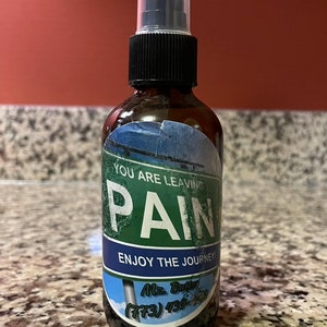 May include: A brown glass bottle with a black spray nozzle and a blue and green label that reads "You are leaving pain. Enjoy the journey!"  The label also includes the text "Mz. Butter (773) 439-7500".