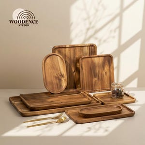 May include: A collection of wooden serving trays in various shapes and sizes. The trays are made of a light brown wood and include rectangular, oval, and square designs. A small glass jar with a lid and gold utensils are also present.
