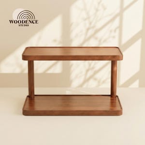 Puede incluir: Una mesa auxiliar de madera rectangular de dos niveles con bordes redondeados. La mesa es de color marrón cálido y tiene un estante inferior. El logotipo "WOODENCE STUDIO" está en la esquina superior izquierda.