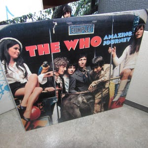 May include: Vintage album cover for "The Who" featuring the band and women in a bus-like setting. The album title "Amazing Journey" is displayed with the band's name in large red letters. The cover has a retro aesthetic.