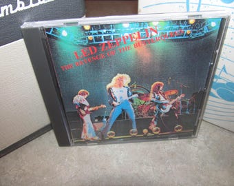 May include: A CD case featuring the band Led Zeppelin. The album cover displays the band members performing on stage under stage lights. The album title "The Revenge of the Buther Roll" is printed in red.