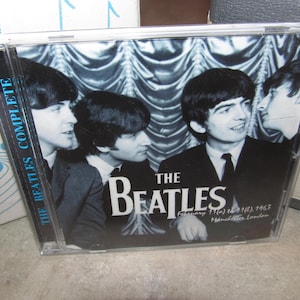 Könnte beinhalten: Eine CD-Hülle mit einem Schwarz-Weiß-Bild der Beatles. Die Bandmitglieder tragen Anzüge und Krawatten, mit dem Bandnamen prominent dargestellt. Der Text "THE BEATLES COMPLETE" befindet sich auf dem Rücken.