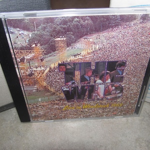 May include: A CD case featuring a concert image with a large crowd and stage. The text "The Who" is prominently displayed, along with "Live at Woodstock 1969". The case is in a clear plastic jewel case.