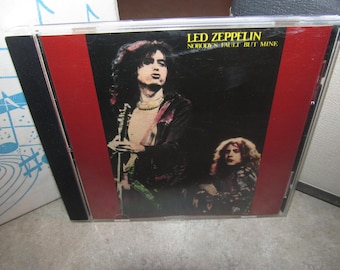 May include: A CD case featuring the Led Zeppelin album "Nobody's Fault But Mine." The cover art displays two band members in a dark setting with a red vertical stripe. The CD case is in a clear plastic jewel case.