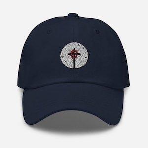 May include: A navy blue baseball cap with an embroidered white circle design featuring a red cross and the text "M.P.S.S.D.N."
