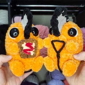May include: Two orange crochet figures of Pochi the Chainsaw Puppy, with black chainsaw details and large eyes. One holds a toast-shaped item with red filling, the other a black and yellow chainsaw. Text reads "Pochi the Chainsaw Puppy".