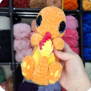 May include: An orange crocheted plush toy of a cartoon character with large black eyes and a yellow belly. The text "Char the cuddly tail monster" is above the toy. The pattern is by Saren Bowie.