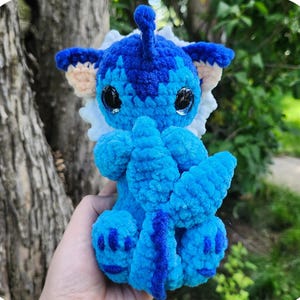 May include: A handmade blue crochet monster toy with the text "Misty the cuddly tail monster." The toy has large black eyes, blue and white accents, and a long tail. The pattern is by Saren Bowie.