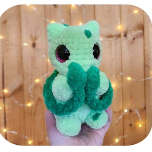 May include: A light green crocheted plush monster with dark green accents, large black glittery eyes, and a rounded head. The text Bulba the cuddly tail monster, Pattern by Saren Bowie, and s_c.handmade are visible in the image frame.