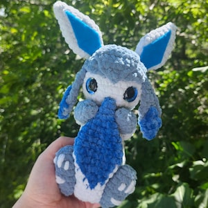 May include: A handmade crochet monster named Glacy, with blue and white plush yarn. The monster has large blue ears, a blue tail, and white accents. The text "Glacy the cuddly tail monster" is at the top.