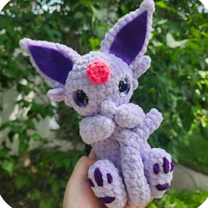 May include: A handmade, lavender-colored crochet monster toy named Espy. It has large, purple-lined ears, a pink nose, and dark purple accents on its paws. The text "Espy the cuddly tail monster" is at the top.