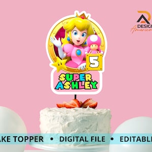 Puede incluir: Un adorno para pastel con un personaje de princesa rosa de la franquicia Super Mario. El personaje sostiene un hongo rosa y un cartel que dice "5". El adorno también incluye el texto "Super Ashley".