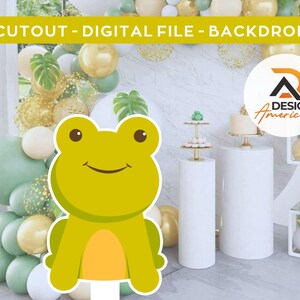 Puede incluir: Un recorte de rana verde con cuerpo amarillo y vientre naranja. La rana está sentada sobre una superficie blanca. El fondo es un telón de fondo de fiesta con globos verdes y dorados, un pastel blanco y una mesa blanca con base dorada.