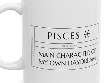 Könnte beinhalten: Ein weißer Keramikbecher mit einem schwarzen, rechteckigen Aufdruck. Der Text lautet PISCES mit dem Tierkreiszeichen, FEB 19 - MAR 20, und MAIN CHARACTER OF MY OWN DAYDREAM. An der Seite steht vertikal der Text ZODIAC COLLECTION.