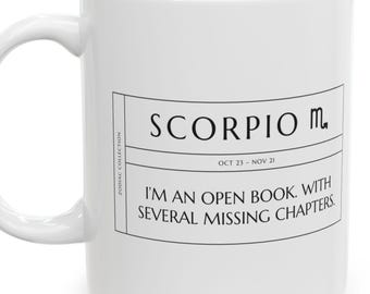 May include: A white ceramic mug featuring a black rectangular graphic with the text SCORPIO, the Scorpio zodiac symbol, the dates OCT 23 - NOV 21, and the phrase I'M AN OPEN BOOK. WITH SEVERAL MISSING CHAPTERS. The text ZODIAC COLLECTION is vertical.
