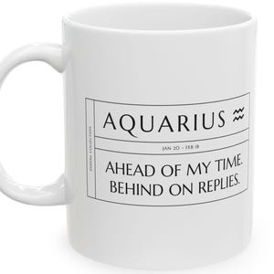 Può includere: Una tazza in ceramica bianca con un design grafico nero che riporta il testo AQUARIUS, il simbolo zodiacale dell'Acquario, le date JAN 20 - FEB 18 e la frase AHEAD OF MY TIME. BEHIND ON REPLIES. Il testo ZODIAC COLLECTION è stampato verticalmente.