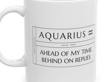 May include: A white ceramic mug featuring a black graphic design with the text AQUARIUS, the Aquarius zodiac symbol, the dates JAN 20 - FEB 18, and the phrase AHEAD OF MY TIME. BEHIND ON REPLIES. The text ZODIAC COLLECTION is printed vertically.