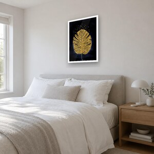 May include: A rectangular wall art print featuring a single large golden monstera leaf centered against a deep black background. The leaf is detailed with fine golden veins and is surrounded by small golden dots at the top edge.