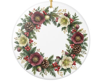 May include: A round white ceramic ornament featuring a printed wreath design. The wreath consists of dark red and pale green hellebore flowers, brown pinecones, green pine needles, and clusters of small red berries. A gold string hangs from the top.