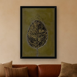 May include: A framed wall art print featuring a large, stylized black leaf with gold-toned vein details centered on a muted olive green background. Above the leaf, a small arc of black dots is arranged in a symmetrical pattern.