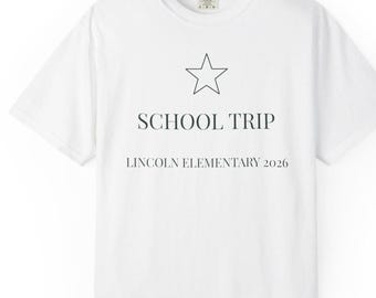May include: A white short-sleeved t-shirt featuring a black outline of a star centred above the text SCHOOL TRIP and LINCOLN ELEMENTARY 2026 in a dark grey serif font. The shirt has a crew neckline and a standard fit with a visible brand label.