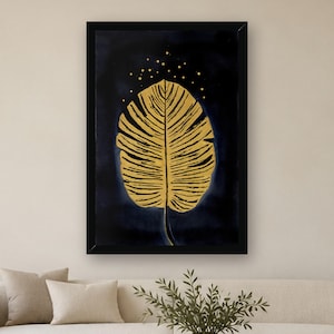 May include: A framed wall art print featuring a large, detailed golden leaf centered against a deep navy blue background. Above the leaf, small golden dots are scattered, creating a subtle speckled effect within the black frame.