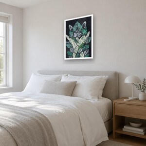 May include: A rectangular wall art print featuring a vertical arrangement of overlapping leaf shapes in shades of dark green, light green, and white against a black background, framed in a simple white border.