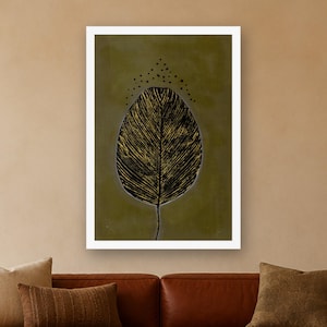 May include: A rectangular wall art print featuring a large, stylized black leaf with visible gold-toned vein details centered on a muted olive green background. Above the leaf, a small arc of black dots is arranged in a triangular pattern.