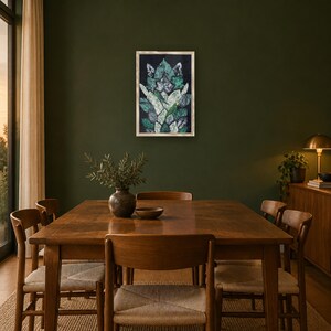 May include: A rectangular framed wall art piece featuring a stylized, symmetrical botanical pattern in shades of dark green, white, and black. The artwork is displayed on a dark olive green wall above a wooden dining table and chairs.