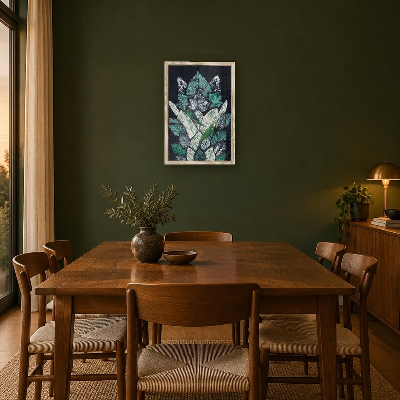 May include: A rectangular framed wall art piece featuring a stylized, symmetrical botanical pattern in shades of dark green, white, and black. The artwork is displayed on a dark olive green wall above a wooden dining table and chairs.