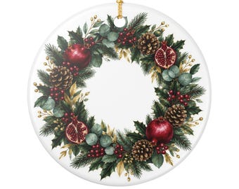 May include: A round white ceramic ornament featuring a printed wreath design. The wreath consists of dark green pine needles, holly leaves, brown pinecones, red berries, and whole and halved pomegranates. A gold string is attached at the top.