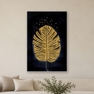 May include: A rectangular wall art print featuring a large, textured golden leaf centered against a deep navy blue background. Above the leaf, small golden dots are scattered, creating a subtle speckled effect across the dark canvas.
