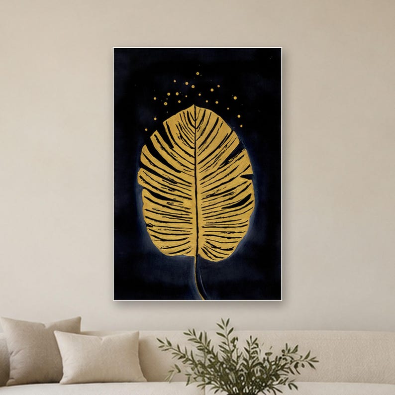 May include: A rectangular wall art print featuring a large, textured golden leaf centered against a deep navy blue background. Above the leaf, small golden dots are scattered, creating a subtle speckled effect across the dark canvas.