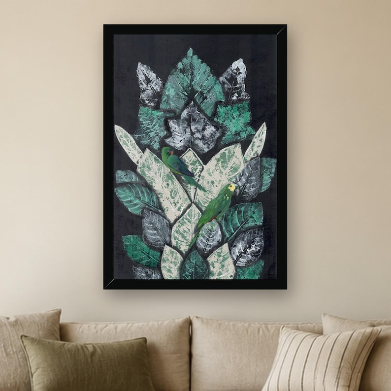 May include: A framed rectangular wall art piece featuring a dark background with a vertical arrangement of layered, textured leaves in shades of green, white, and black. Two small green parrots are perched among the foliage.