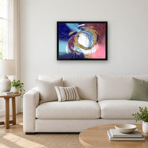 Puede incluir: Una pintura abstracta enmarcada que presenta una pincelada circular dorada central rodeada por capas giratorias de pintura azul profundo, magenta y blanca. La composici&oacute;n incluye goteos verticales de color, todo dentro de un marco negro.