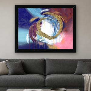 Puede incluir: Una pintura abstracta enmarcada que presenta una pincelada circular dorada central con gotas de pintura. El fondo consta de capas mezcladas de azul profundo, magenta, blanco y azul claro, creando una composici&oacute;n din&aacute;mica y arremolinada.