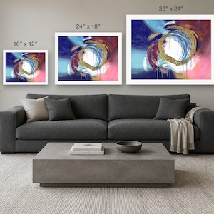 Puede incluir: Tres impresiones de arte mural rectangulares con remolinos abstractos de pintura azul, rosa y dorada. Las impresiones est&aacute;n etiquetadas con dimensiones de 16" x 12", 24" x 18" y 32" x 24", dispuestas en una fila horizontal sobre un sof&aacute; gris.