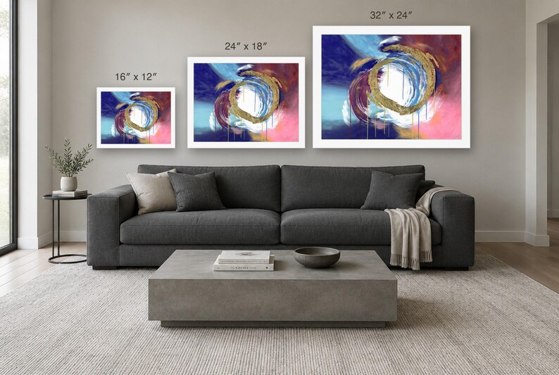 Puede incluir: Tres impresiones de arte mural rectangulares con remolinos abstractos de pintura azul, rosa y dorada. Las impresiones est&aacute;n etiquetadas con dimensiones de 16" x 12", 24" x 18" y 32" x 24", dispuestas en una fila horizontal sobre un sof&aacute; gris.