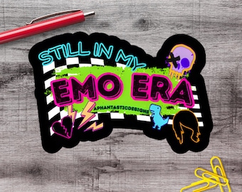 May include: A die-cut sticker featuring a black and white checkered background with a bright green brushstroke. The text reads STILL IN MY EMO ERA in bold black and pink letters. It includes a purple skull, a blue dinosaur, and a broken heart.